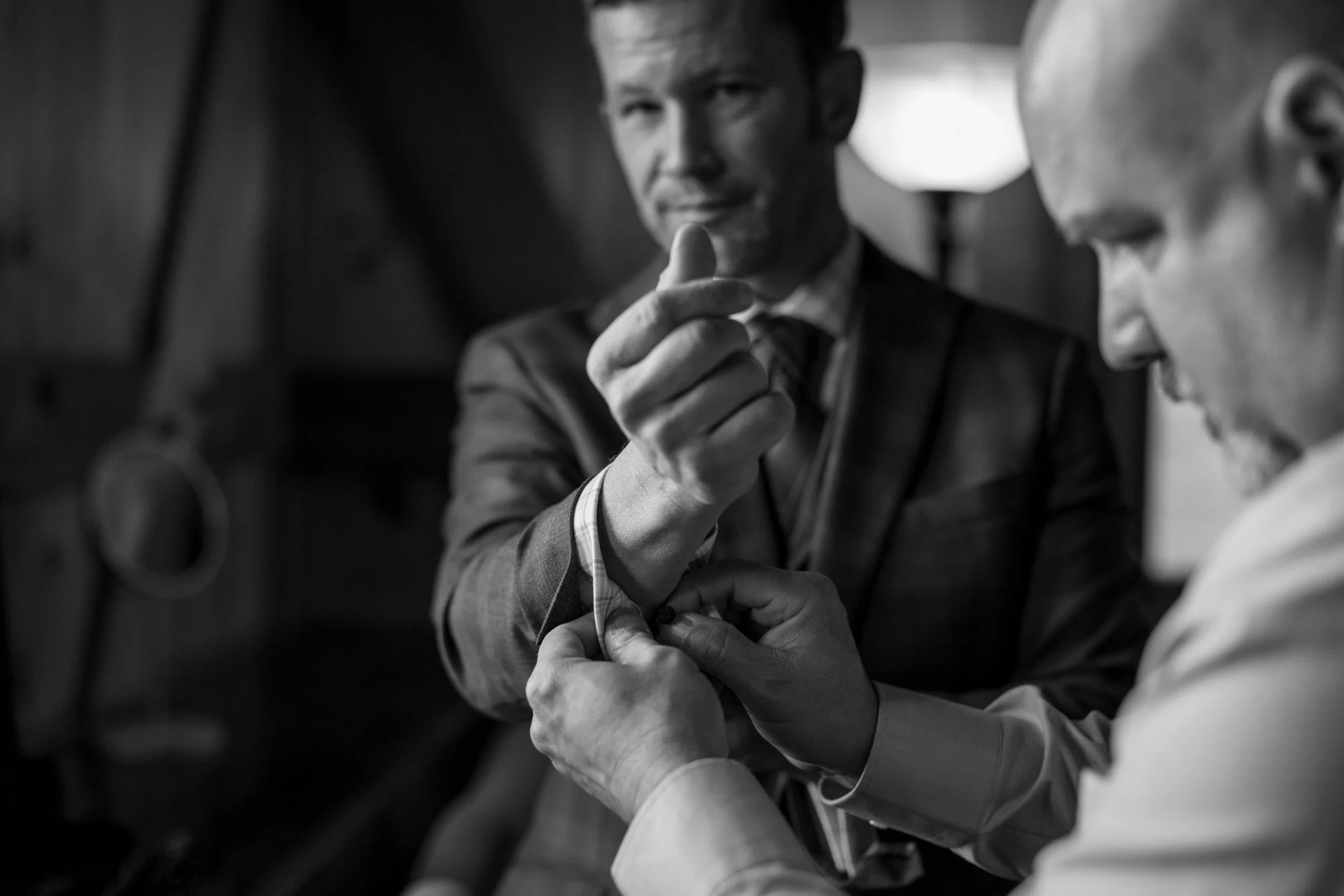 Two businessmen are holding hands in a handshake, with one man's hand over the other's in a gesture of support or agreement. They are in a professional setting.