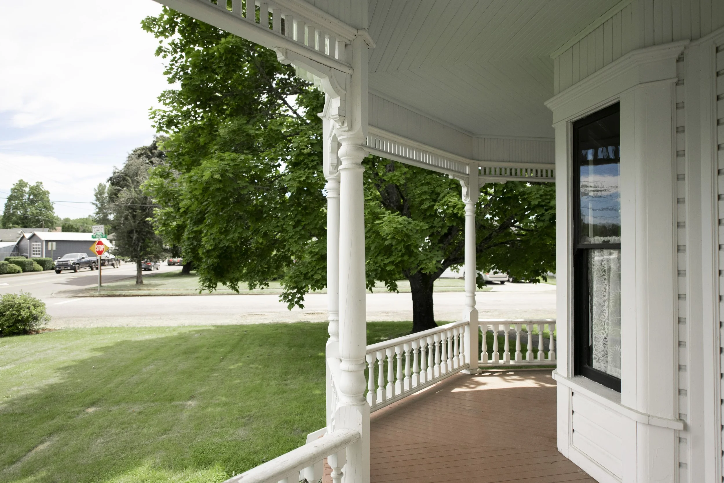 View from the porch of the 1903 Brown House showing white decorative columns and railing, with a tree, street, and houses in the background.