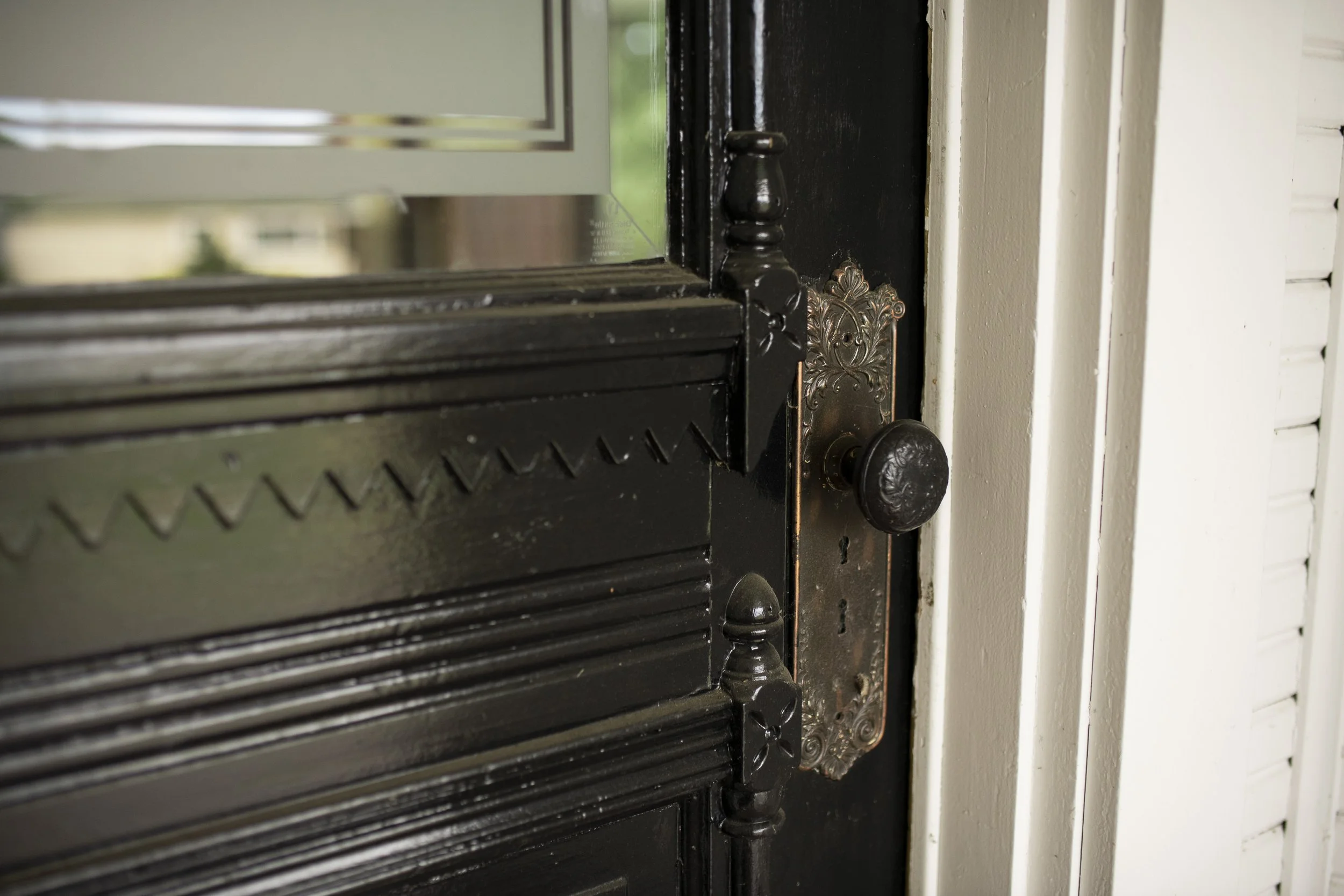 Close-up of a vintage black cast-iron stove with decorative details, situated next to white wooden paneling. One of the fine details of the 1903 Victorian Brown House in Stayton, Oregon.