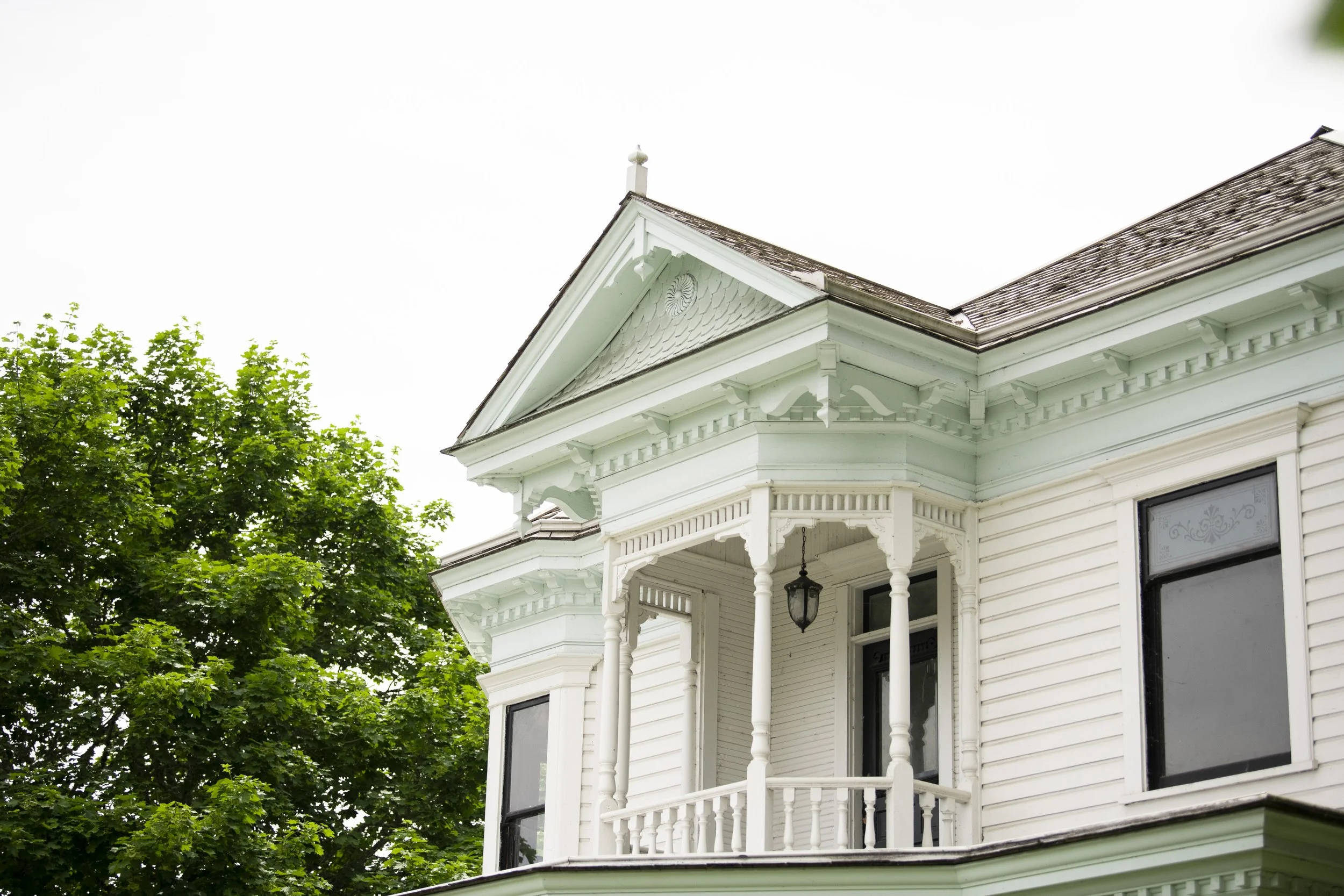 Close-up of the upper section of the Brown House with ornate wood trim and a balcony, surrounded by green trees.