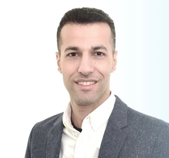 Portrait of a man with short dark hair wearing a gray blazer and white shirt against a white background.