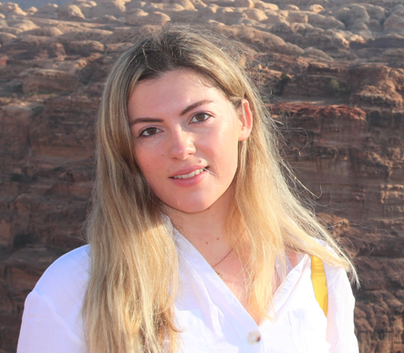 Young woman with long blonde hair standing outdoors with rock formations in the background.