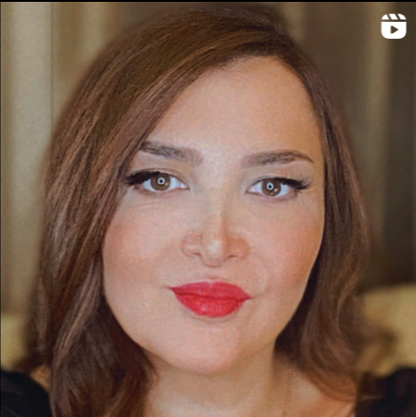 Close-up of a woman with shoulder-length brown hair, red lipstick, and makeup, looking at the camera with a slight smile.