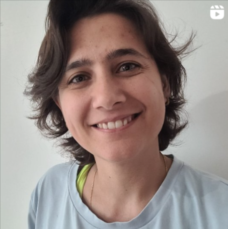 A woman with short, dark brown hair, smiling, wearing a light-colored shirt, in front of a plain white background.
