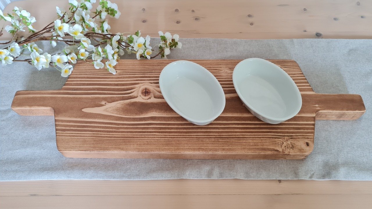 Two white ceramic bowls on a wooden serving board with a sprig of white flowers on the side.
