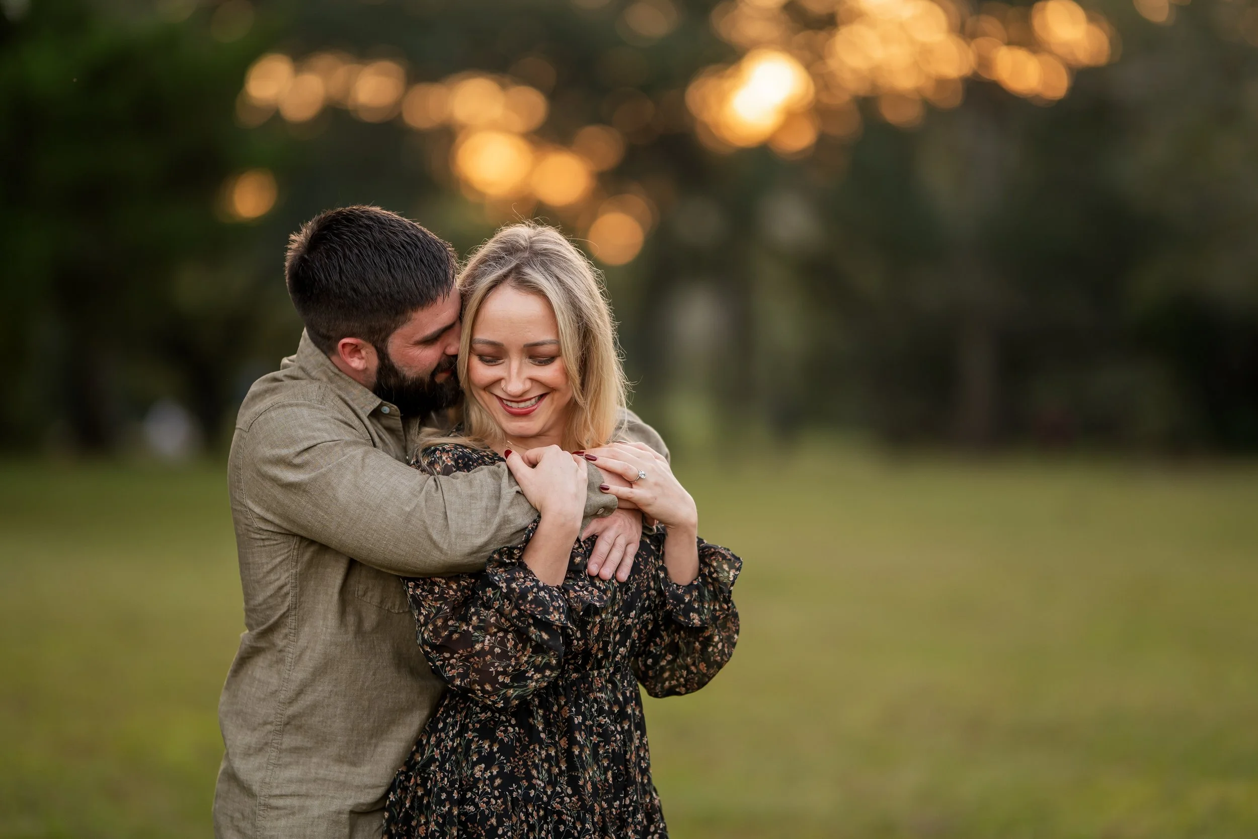 Engaged couple embracing and smiling during an outdoor sunset portrait session near Houston.