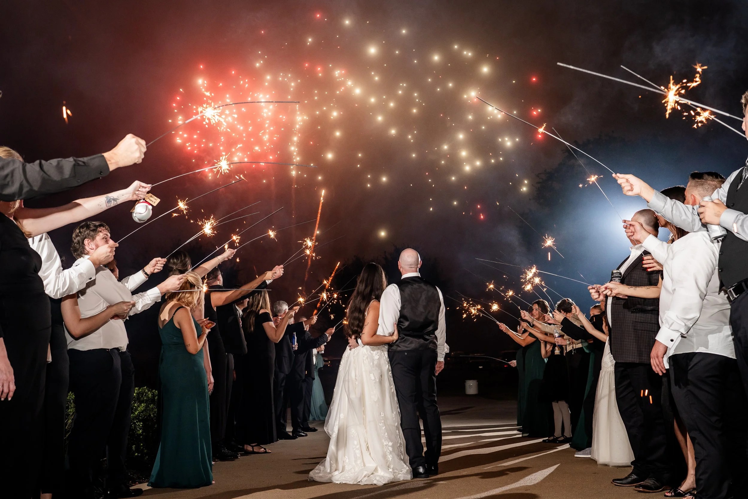Bride and groom walking through a sparkler exit surrounded by wedding guests at night.