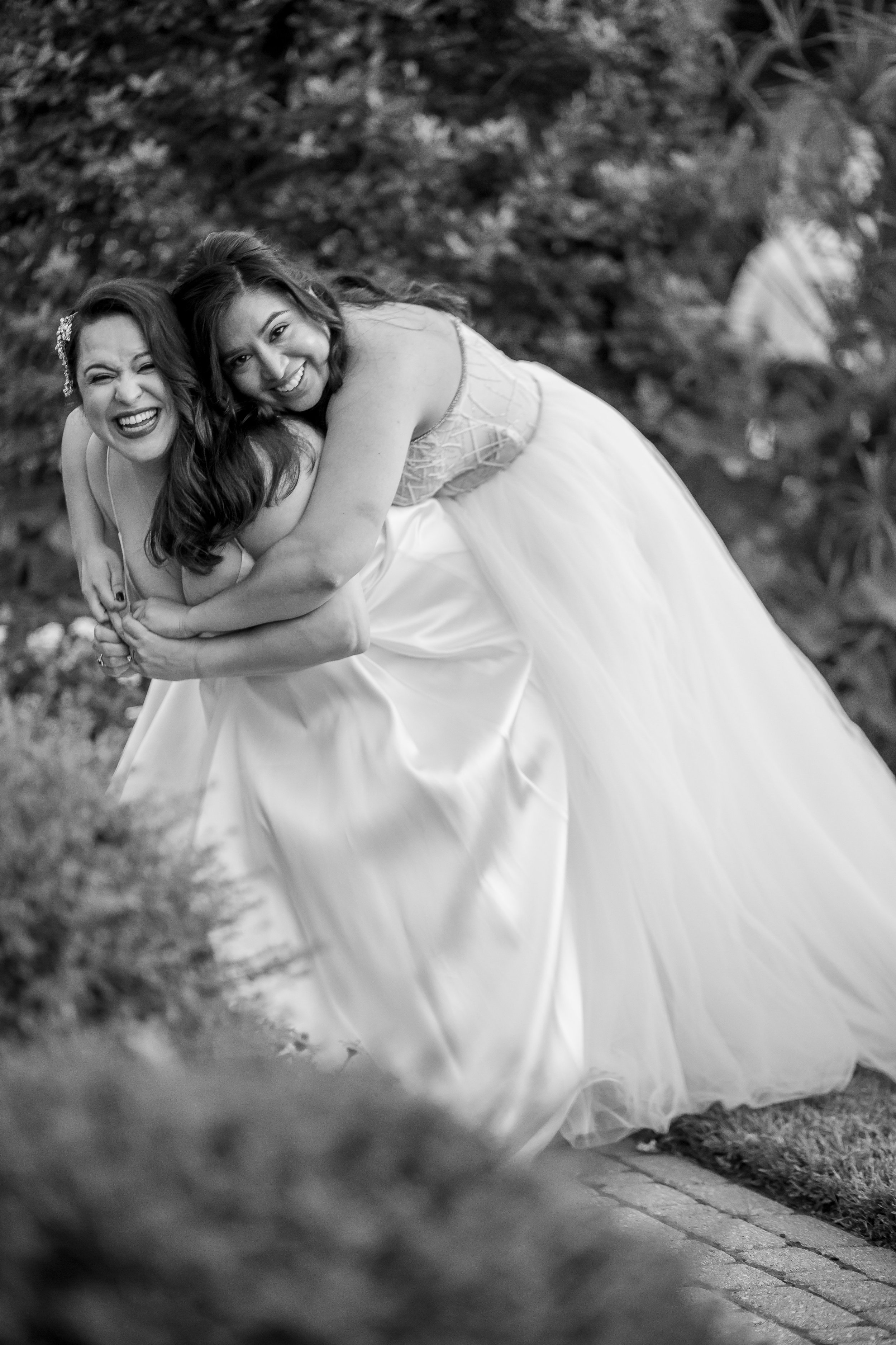 Two brides laugh together during a playful black-and-white wedding portrait.