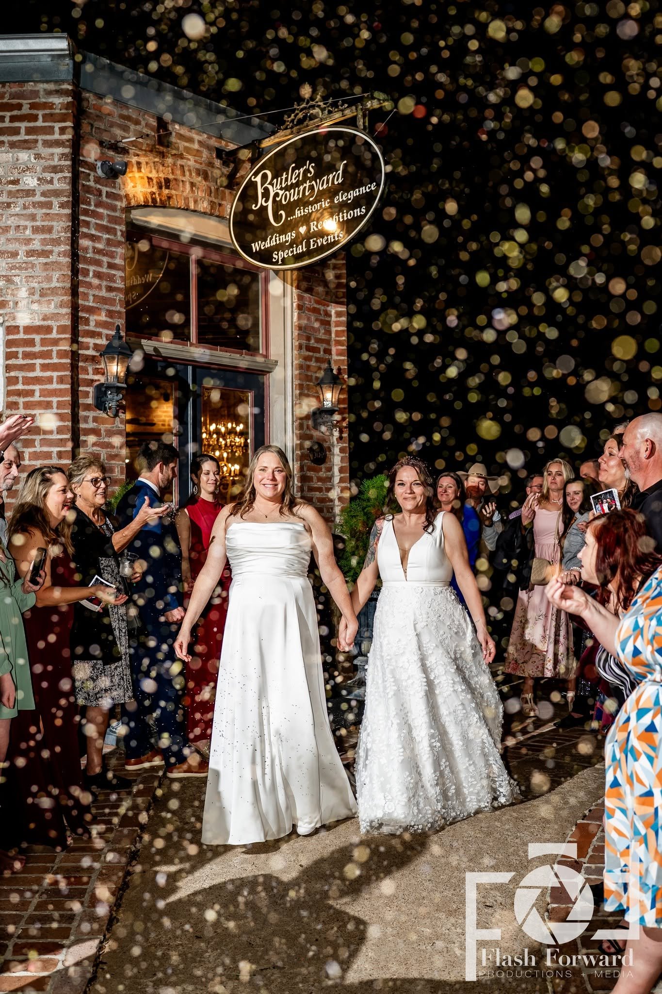Two brides hold hands during a bubble exit outside Butler’s Courtyard as their guests celebrate.
