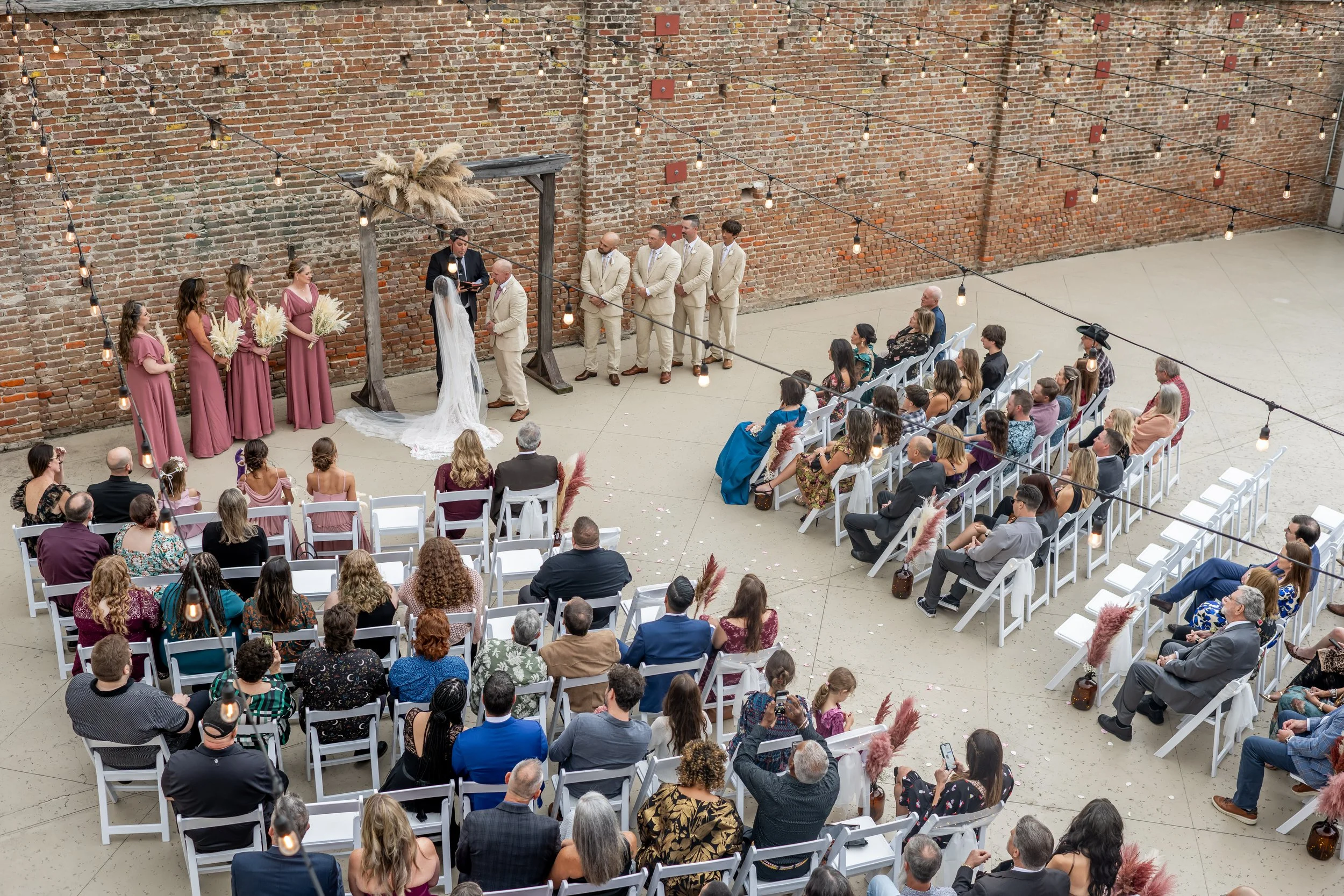 levated view of an outdoor wedding ceremony surrounded by brick walls and hanging string lights.