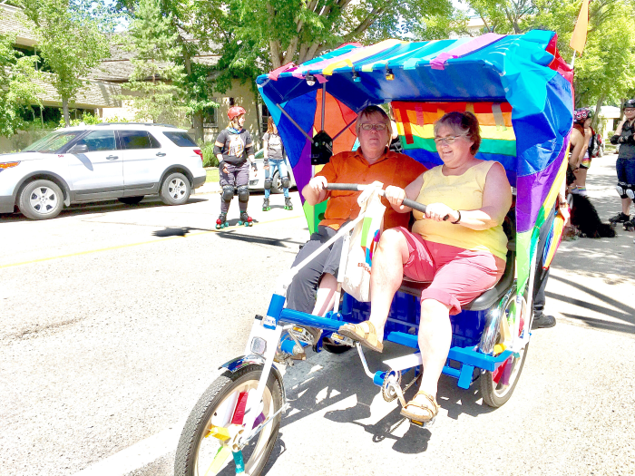 Two women driving a rainbow-decorated double bike. They are laughing.
