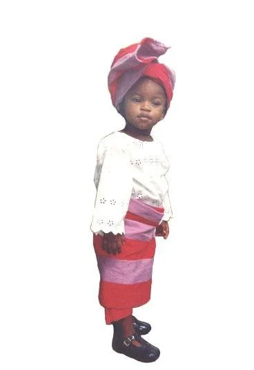 Peace Akintade as a child wearing a white lace blouse, African textile wrap skirt, and matching headwrap.