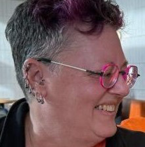 Belinda Betker wears red glasses and is smiling and looking to the right. She has short dark hair.