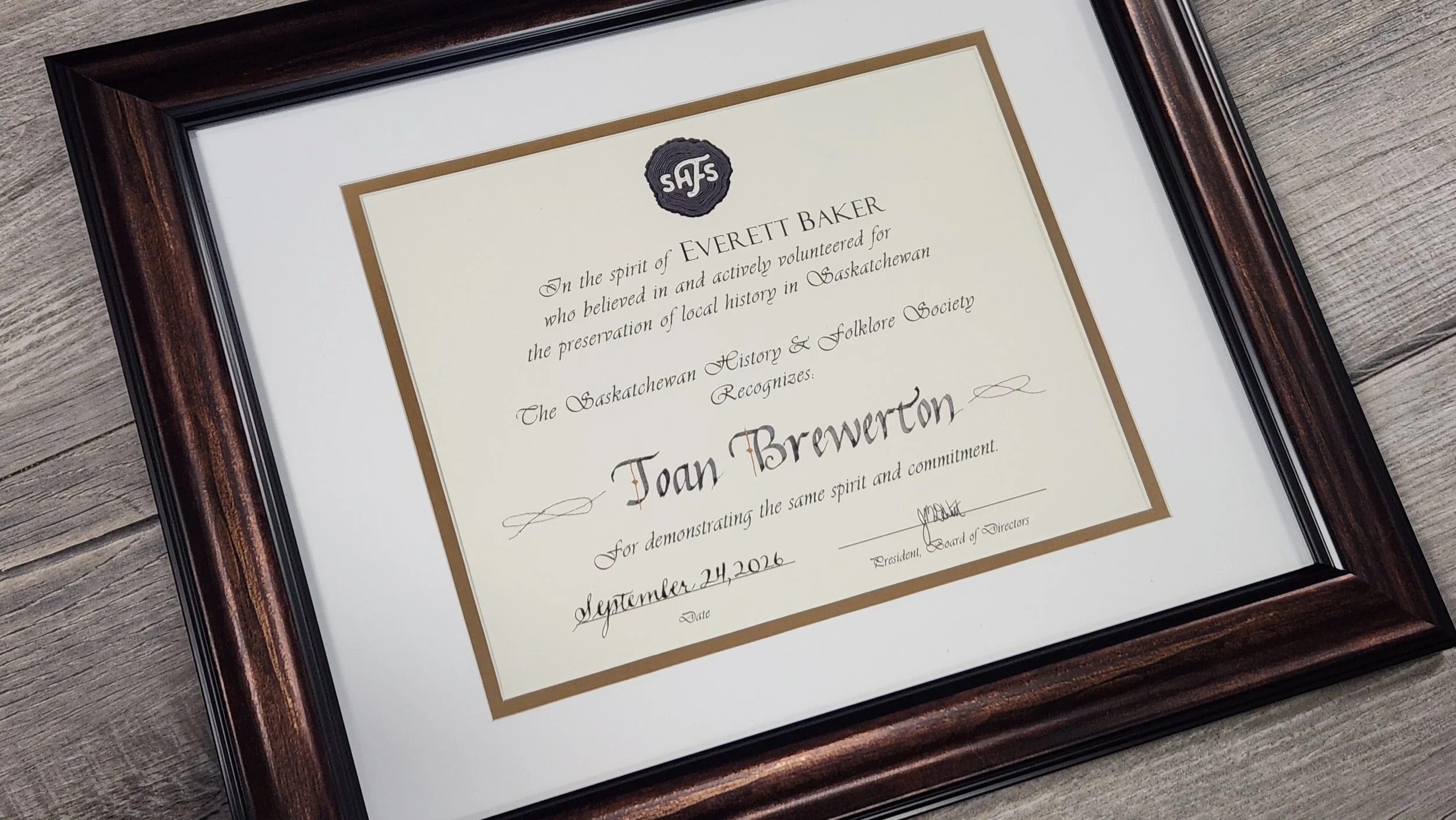 A framed awards certificate reads: In the spirit of Everett Baker who believed in and actively volunteered for the preservation of local history in Saskatchewan/The Saskatchewan History & Folklore Society recognizes Joan Brewerton Sept 24 2026