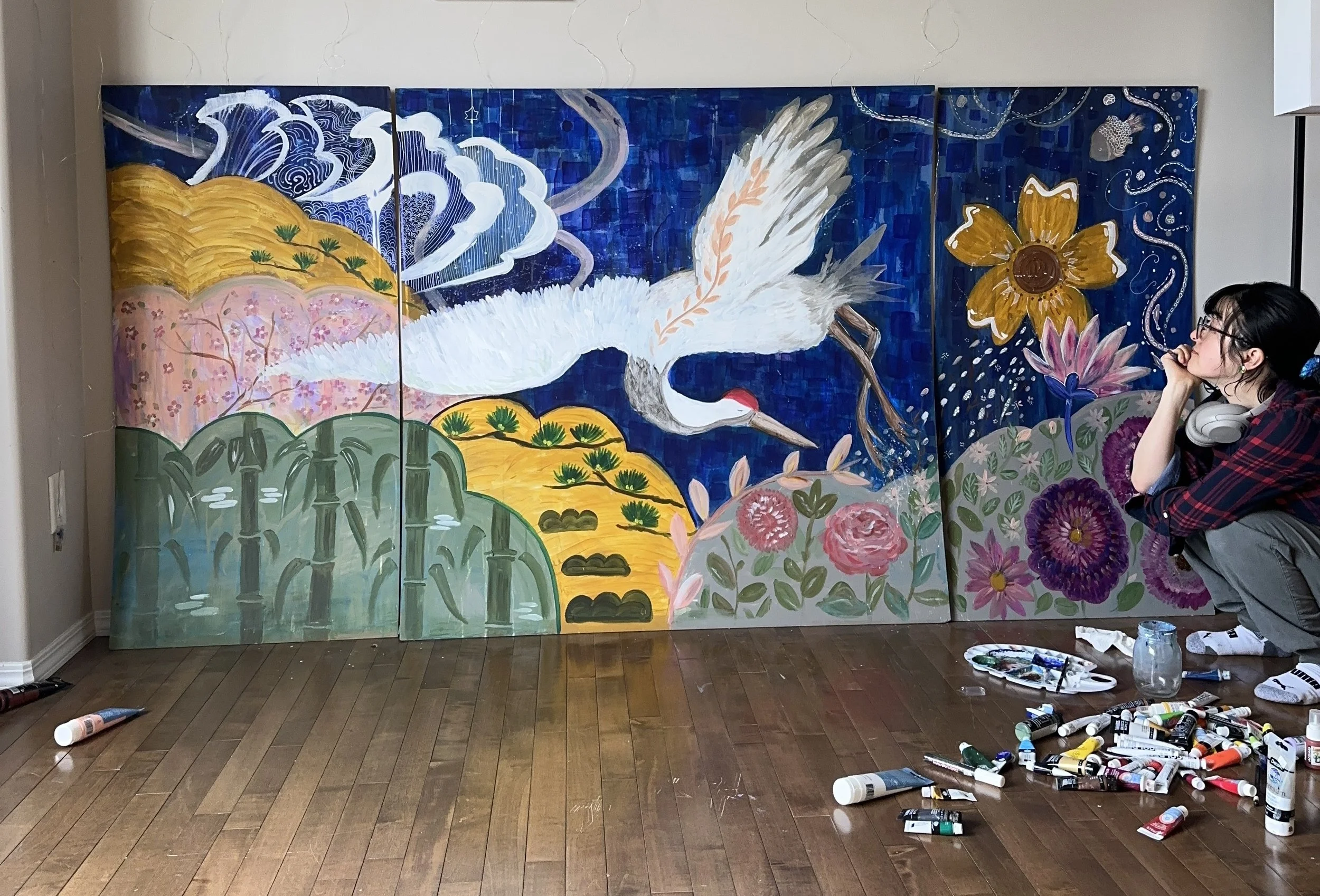 Chikako Ogawa sits in front of a large colorful painting. Acrylic paints are scattered about her feet.