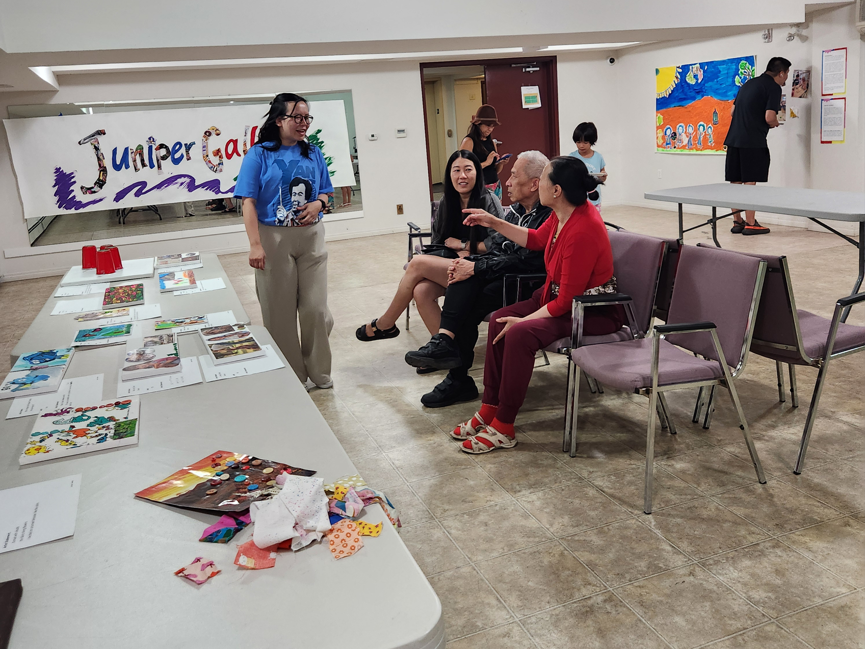 People sit in chairs, talking and smiling. Art is displayed on the walls and the table in front of them.