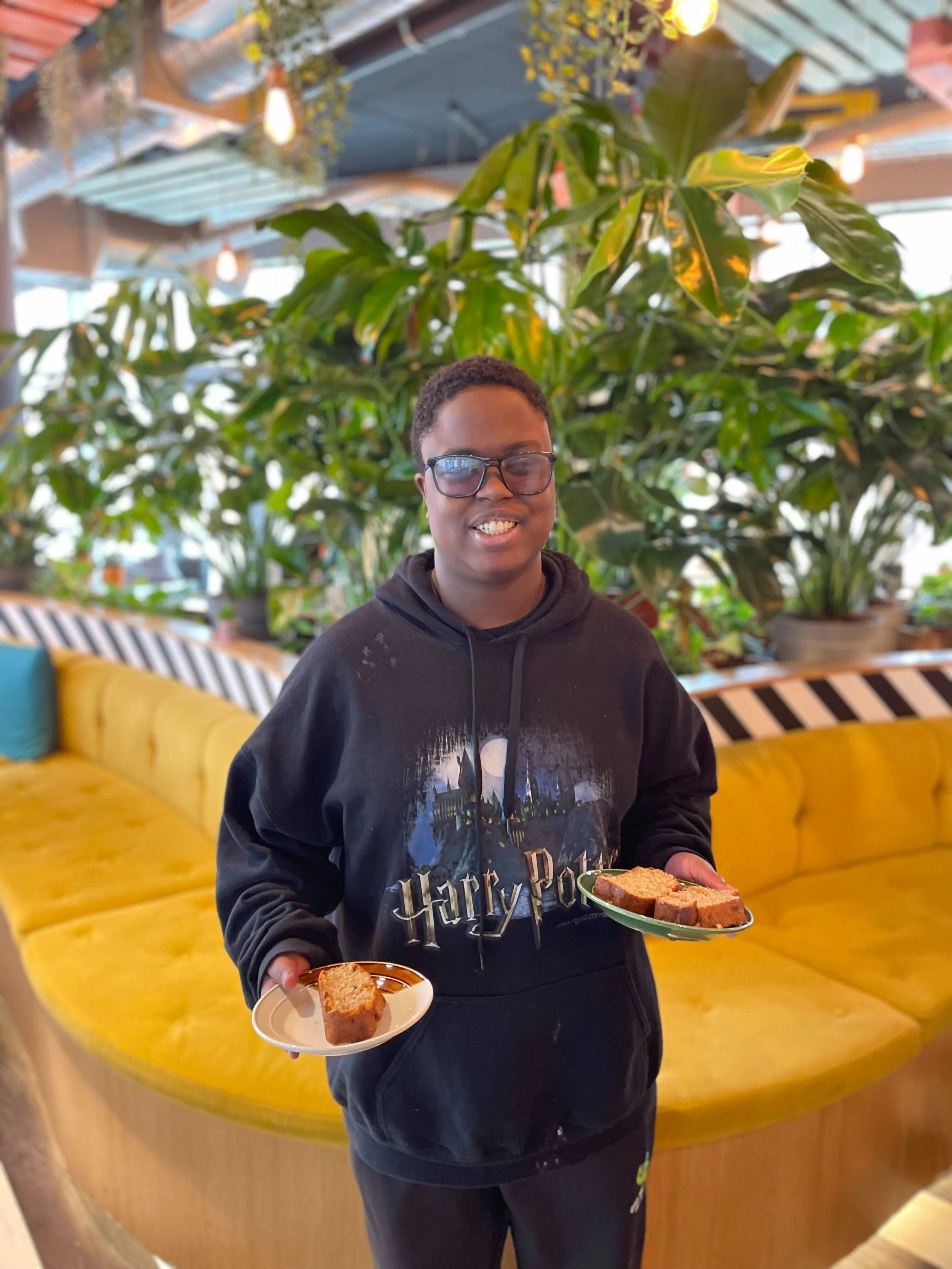 A photograph of a woman in a coffee shop holding two plates of sandwiches.