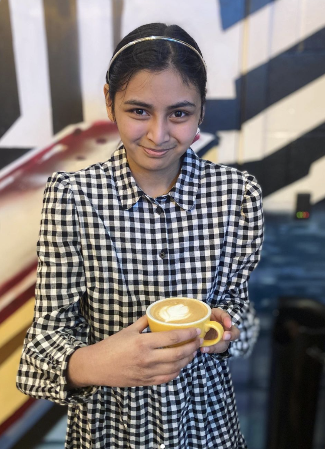 A girl holding a coffee and looking at the camera