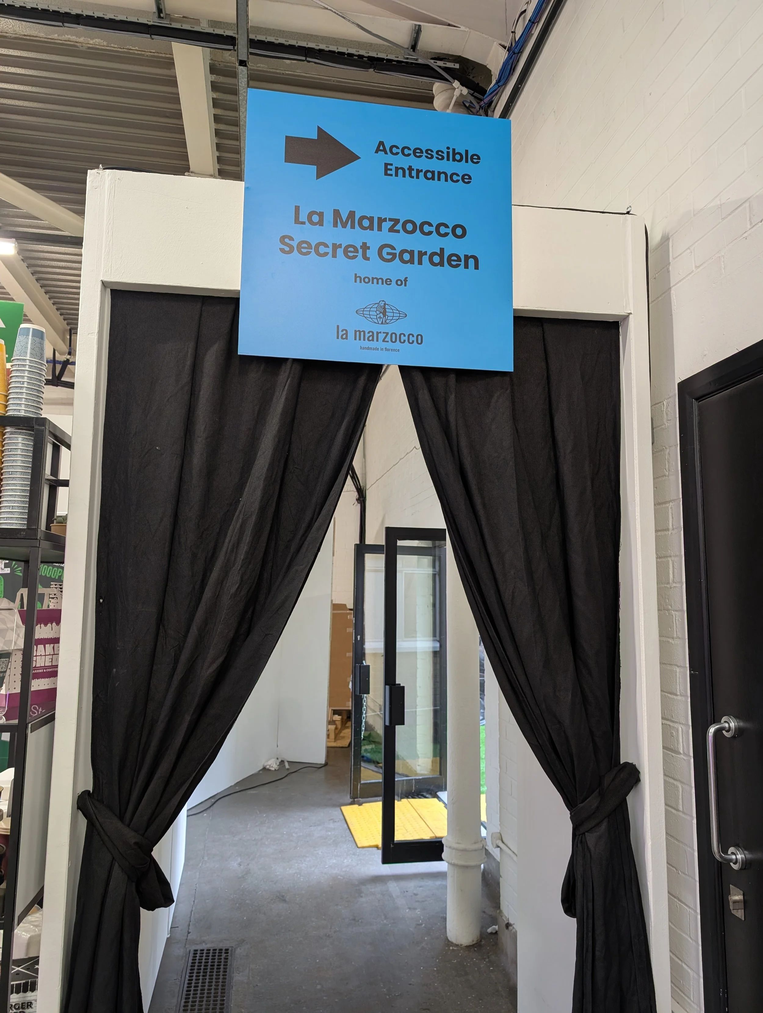 An image showing a blue sign which directs people to the accessible entrance to the secret garden at London Coffee Festival