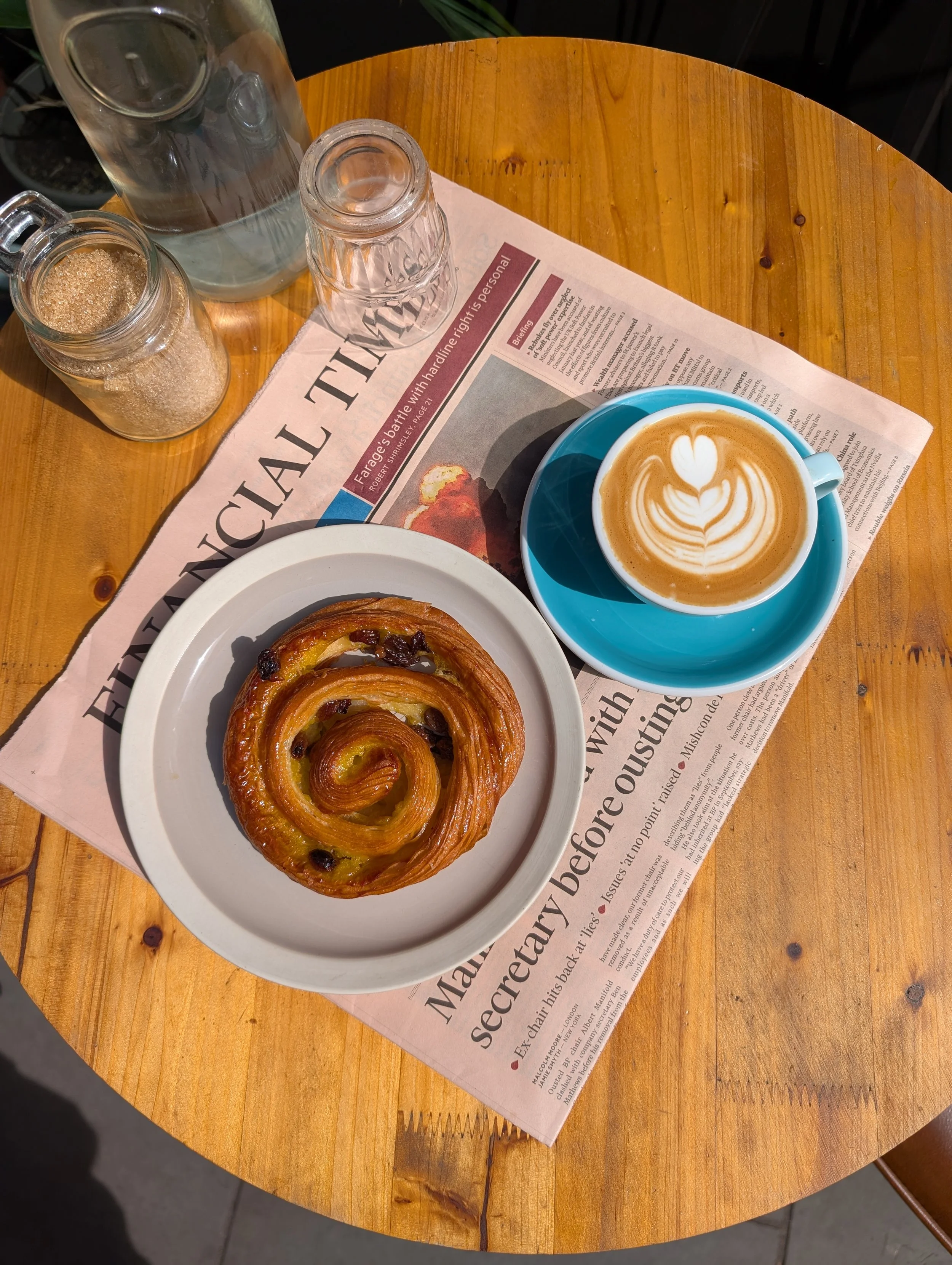 A photo of a pastry and a coffee in the sun on a wooden table