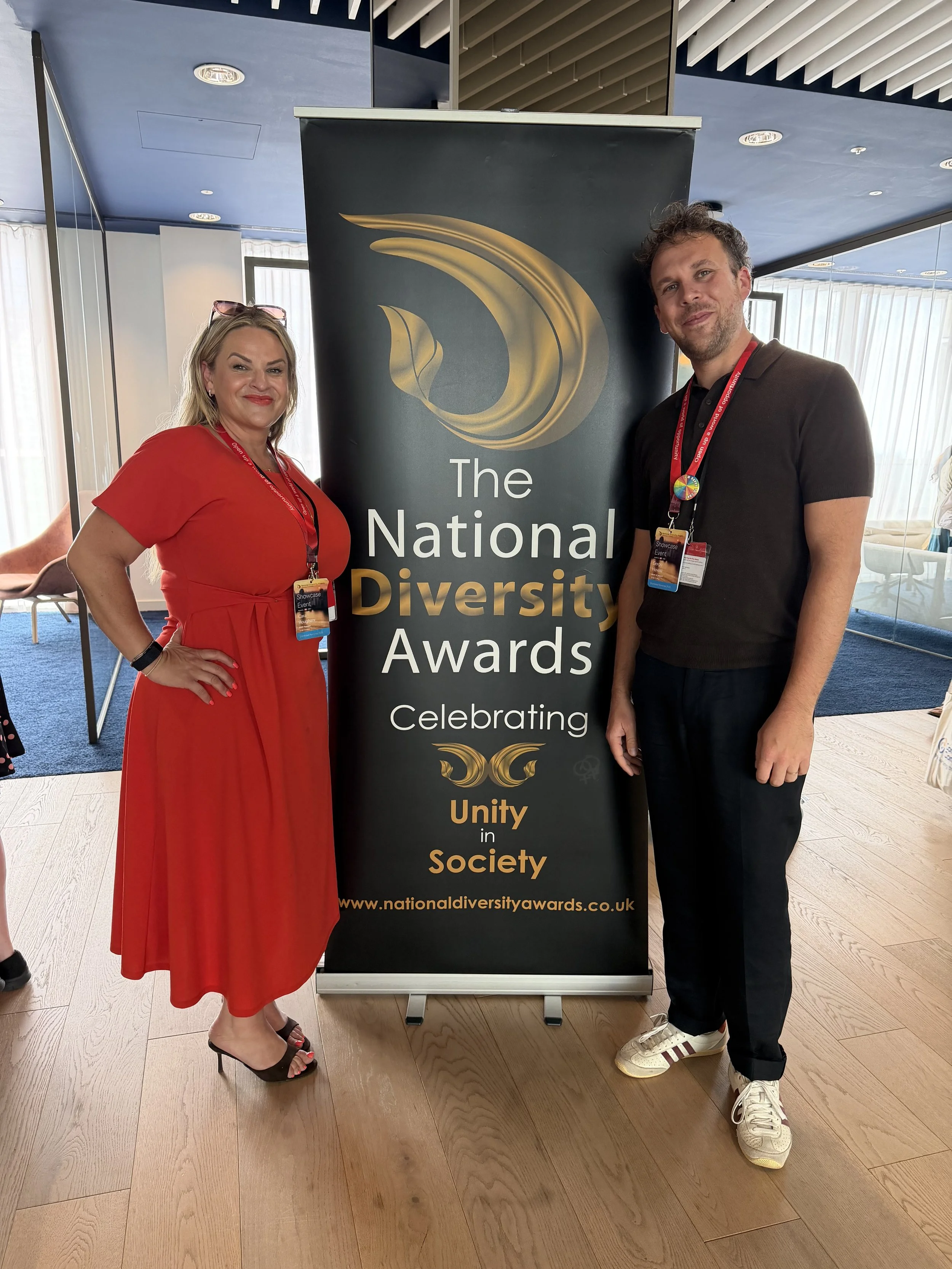 A man and a woman standing next to a banner for the National Diversity Awards