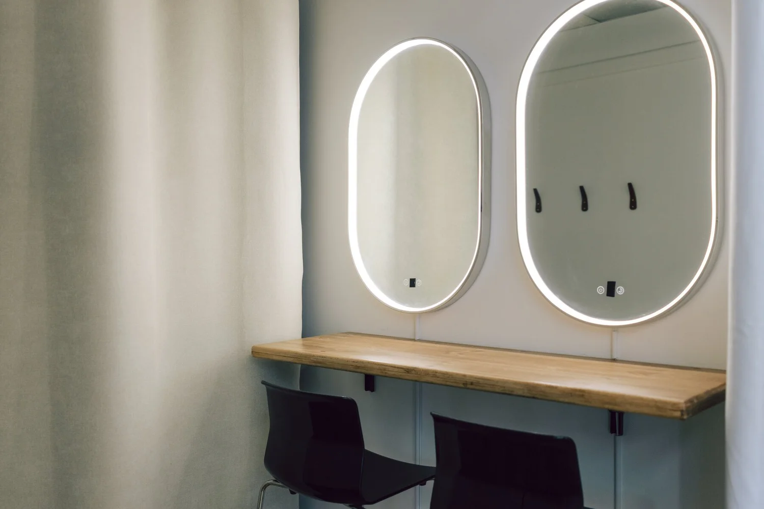 The change area at Nomadic Studio Co., with two lit oval mirrors, a live edge wood counter and stools