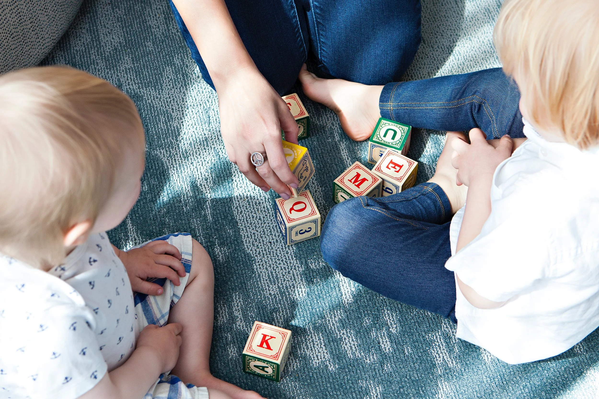 areal photo of two children and a woman playing with letter blocks on a blanket outside