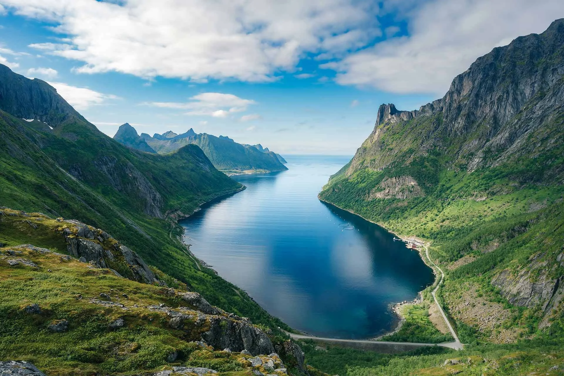 A deep fjord surrounded by steep, green mountains under a partly cloudy sky.
