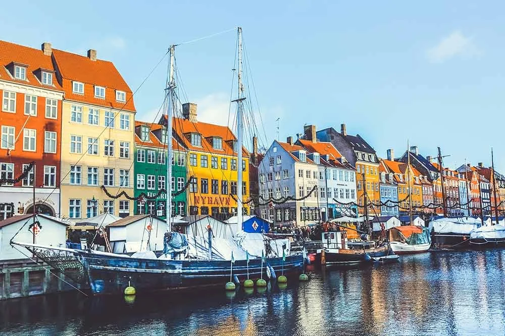 Colorful buildings and sailboats docked along a waterfront in a Scandinavian city.