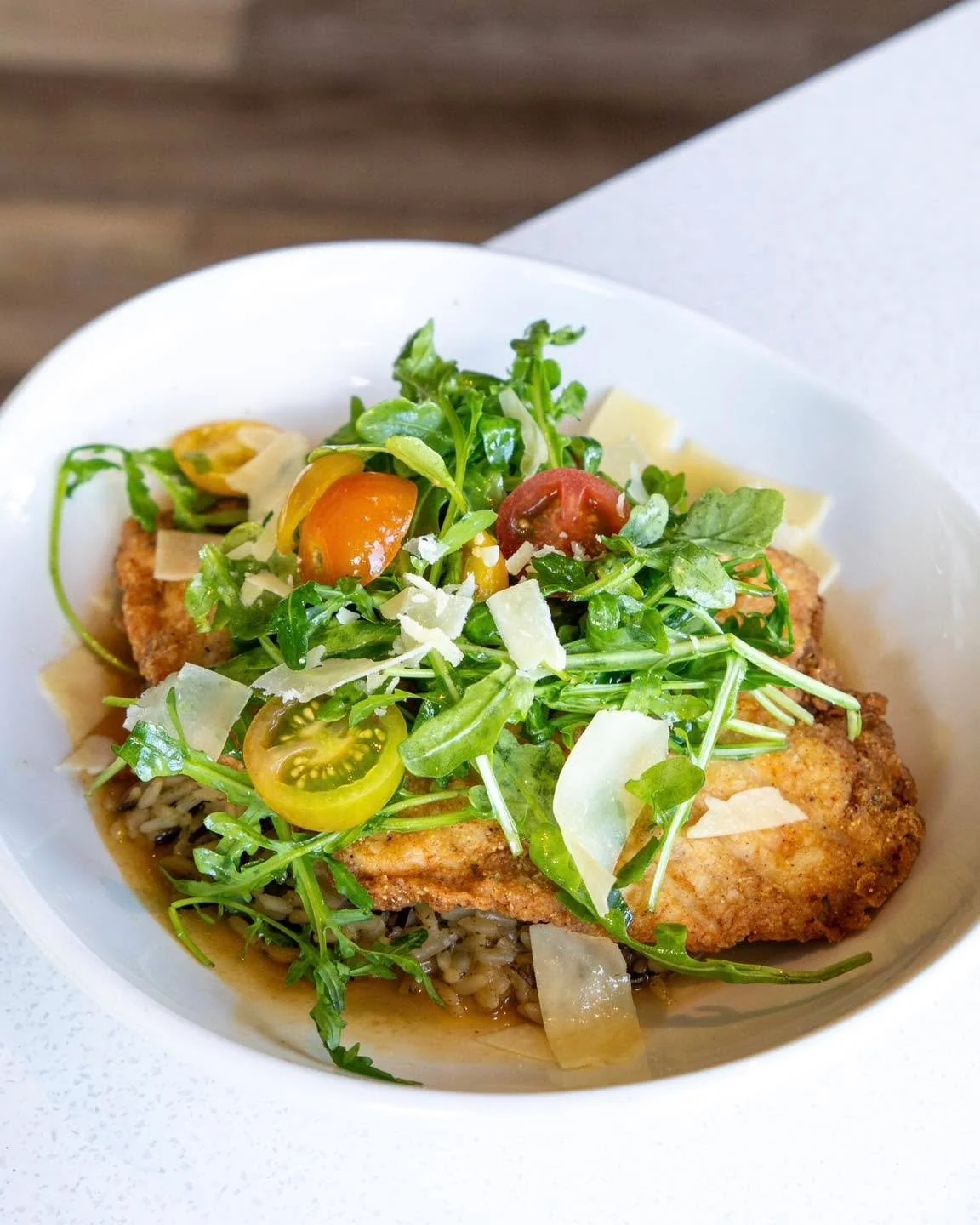 Comfort food with a refined twist. The Chicken Milanese brings together crispy parmesan-crusted chicken, fresh heirloom tomatoes, peppery arugula, wild rice, and a savory chicken jus in every bite.