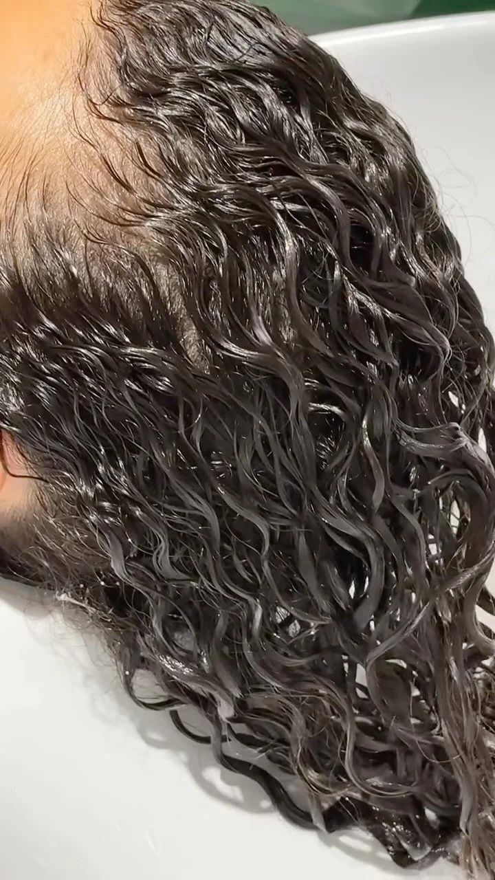 Close-up of dark, wet, curly hair being washed in a hairdressing salon.