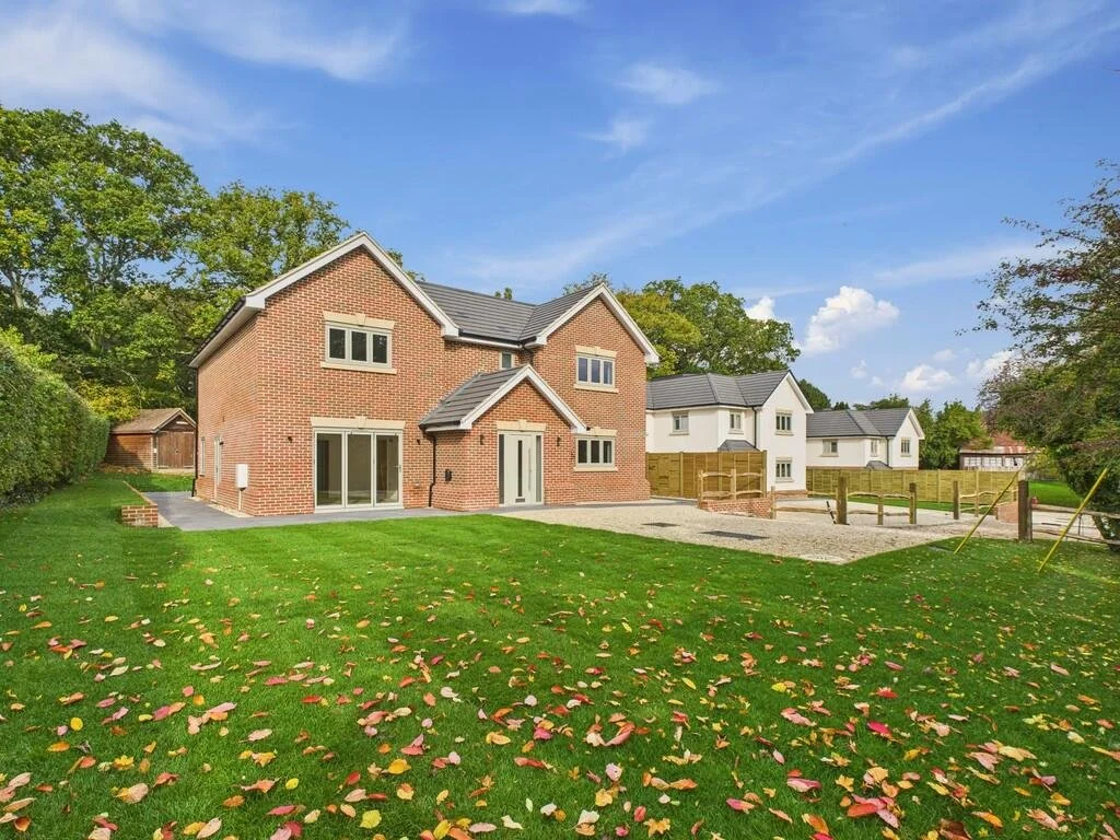 A white cottage with a pitched roof and multiple chimney stacks, located next to a road with trees in the background.