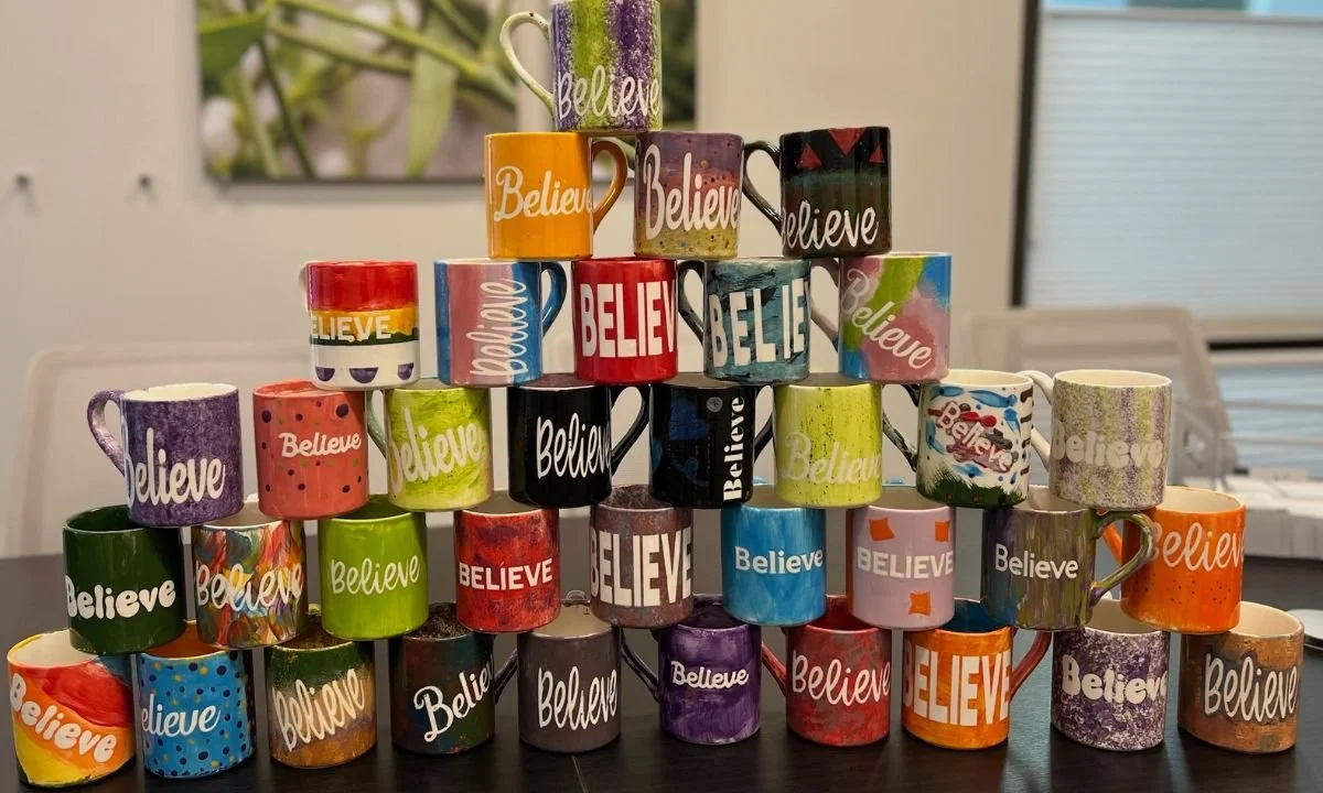 Stack of hand-painted mugs with the word Believe
