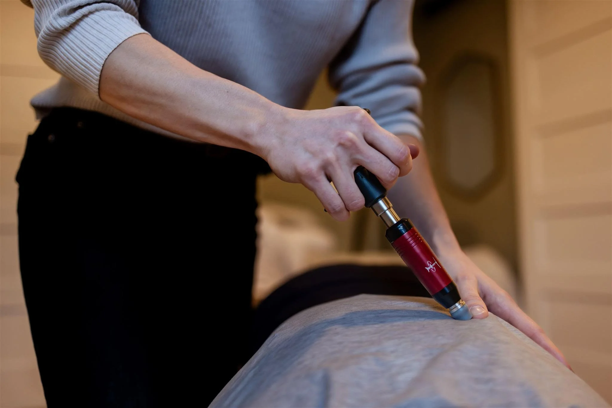 Person using a laser therapy device on a person's back in a treatment room.
