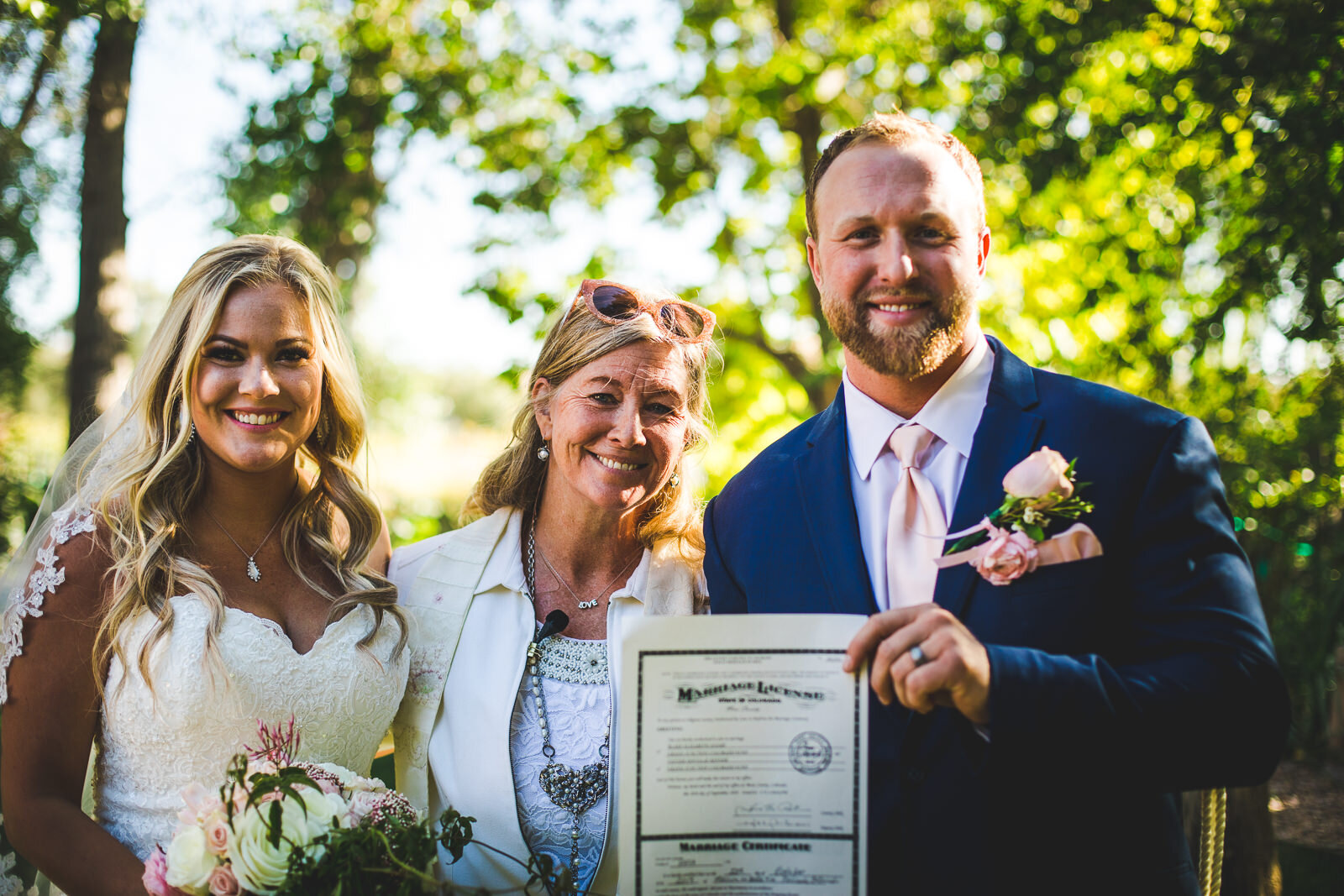 Wedding officiant and celebrant standing between married couple holding the marriage license 