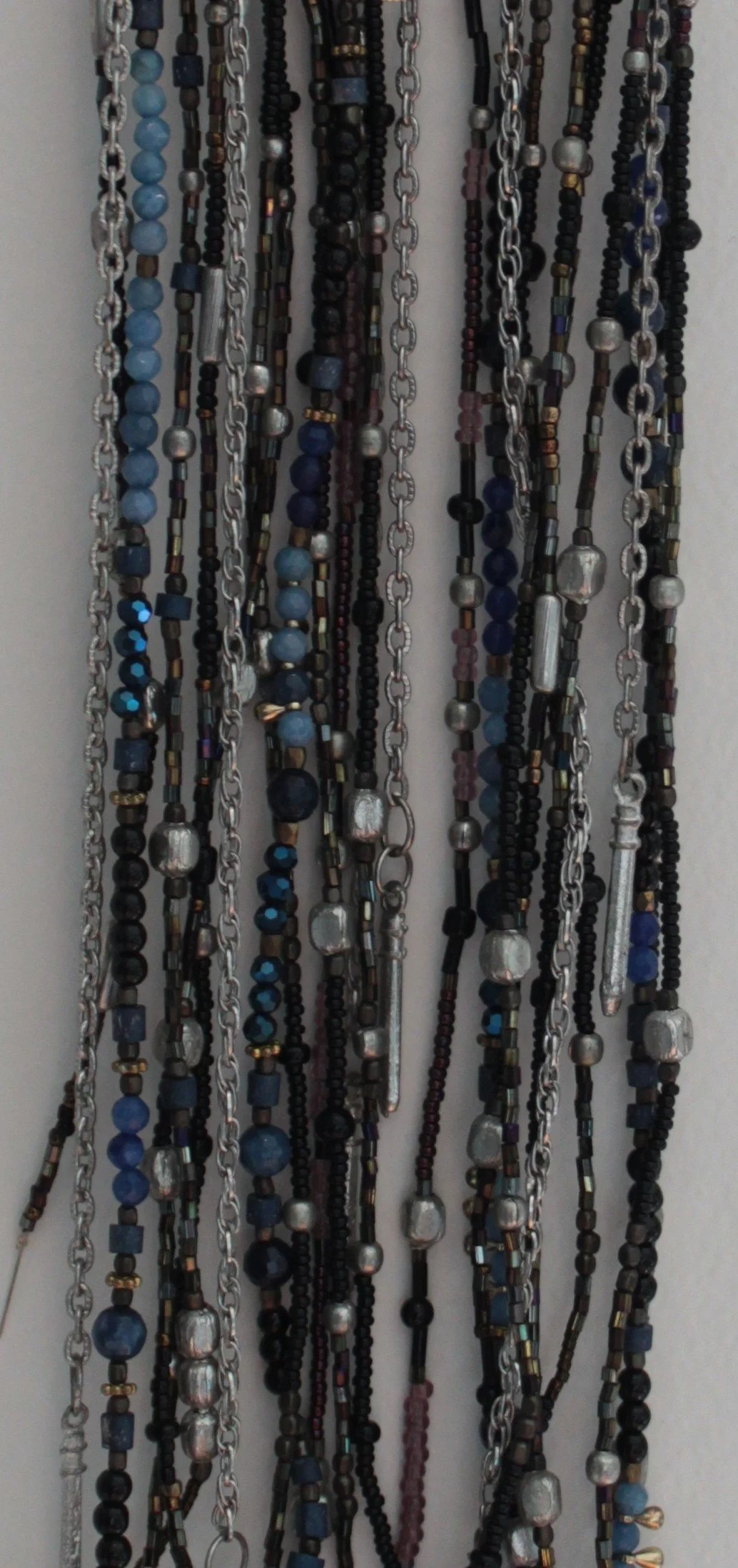 Various beaded necklaces hanging on a wall display, featuring black, blue, silver, and multicolored beads with chains.