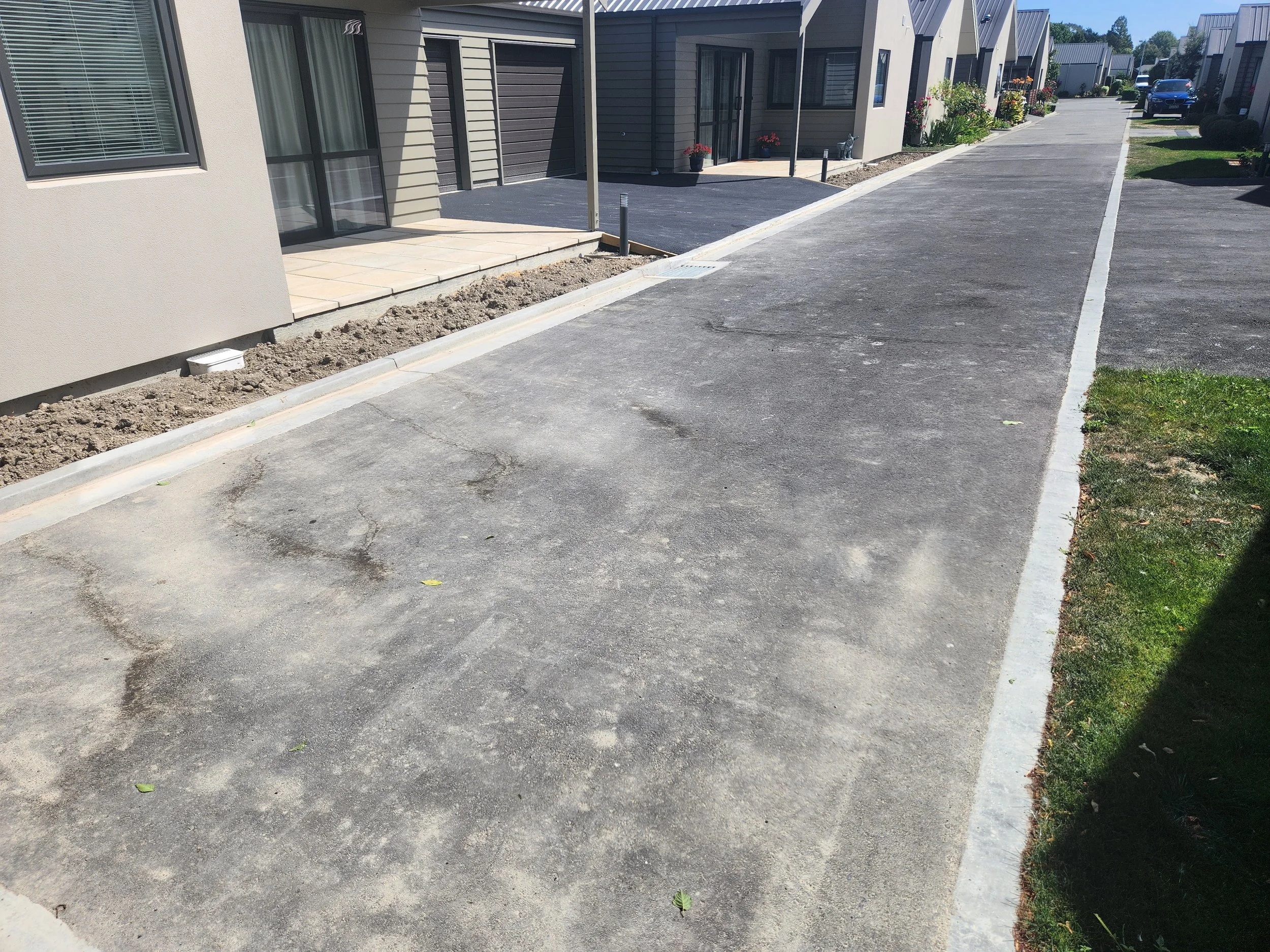 A modern apartment complex with a paved driveway, plants, and flowers in pots near the entrances of the units.