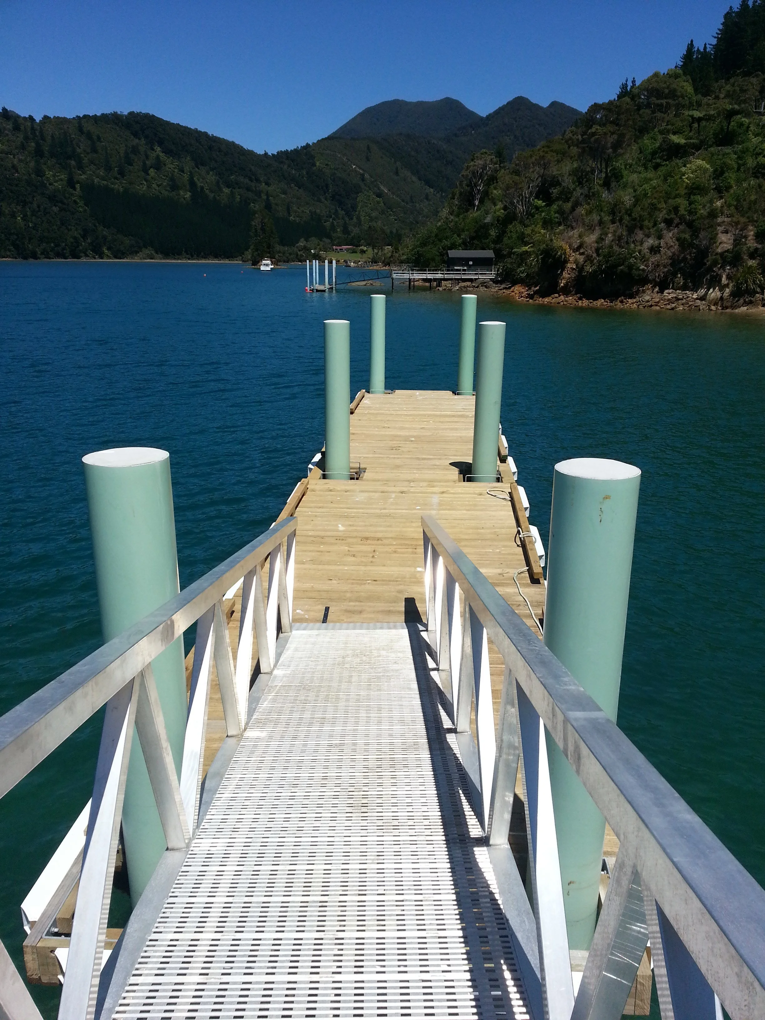 A wooden dock extending over a body of water, with green hills and mountains in the background.