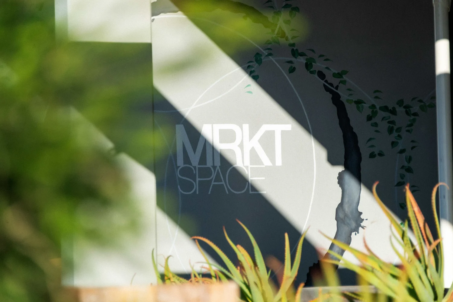 The MRKTSPACE sign framed by green foliage at Leighton Beach