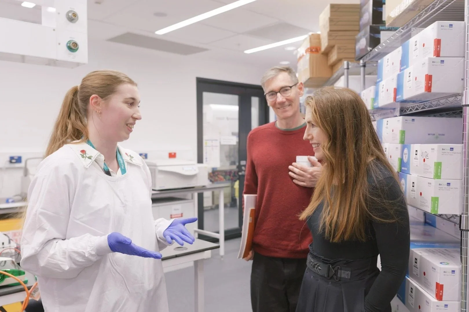 A stem cell researcher in a white lab coat speaking to Patricia Piccinini