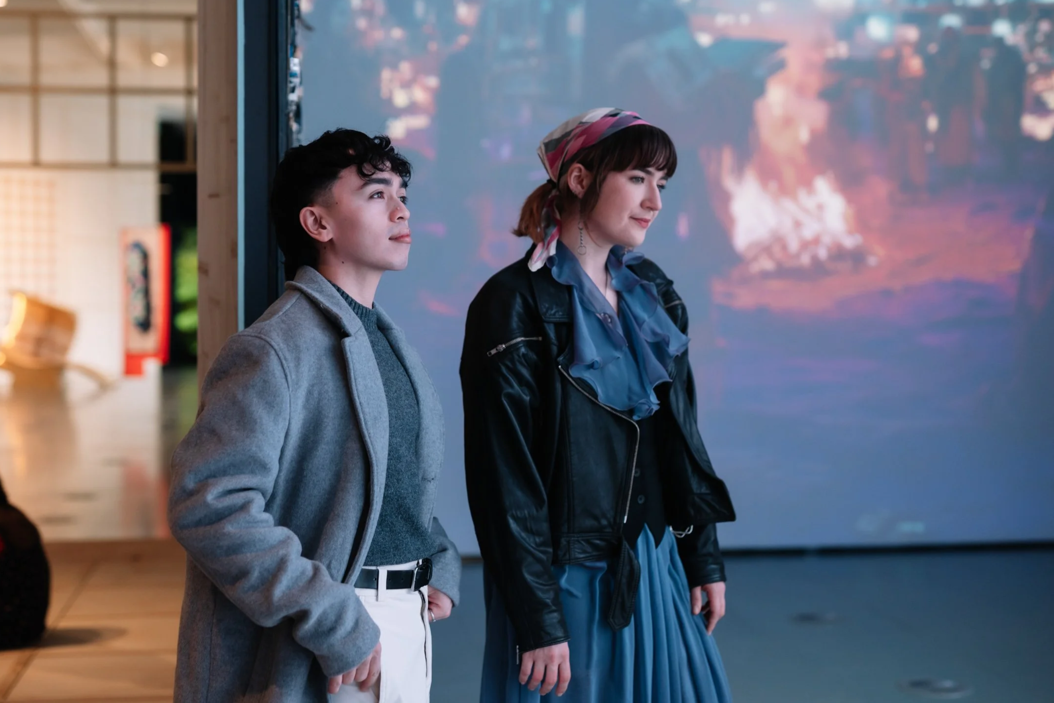 Two people standing in front of a projection artwork, looking to the right.