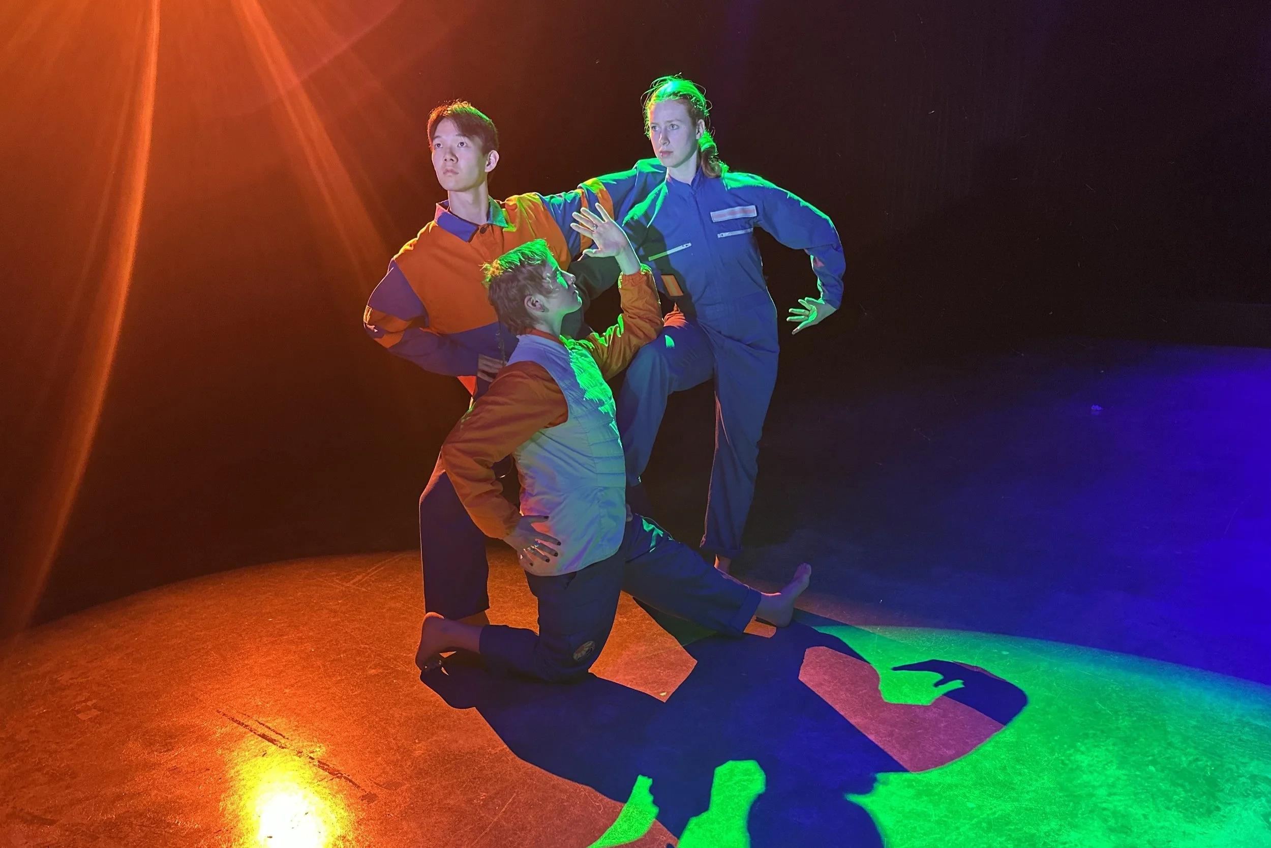 Three performers in a pose under colourful lighting.