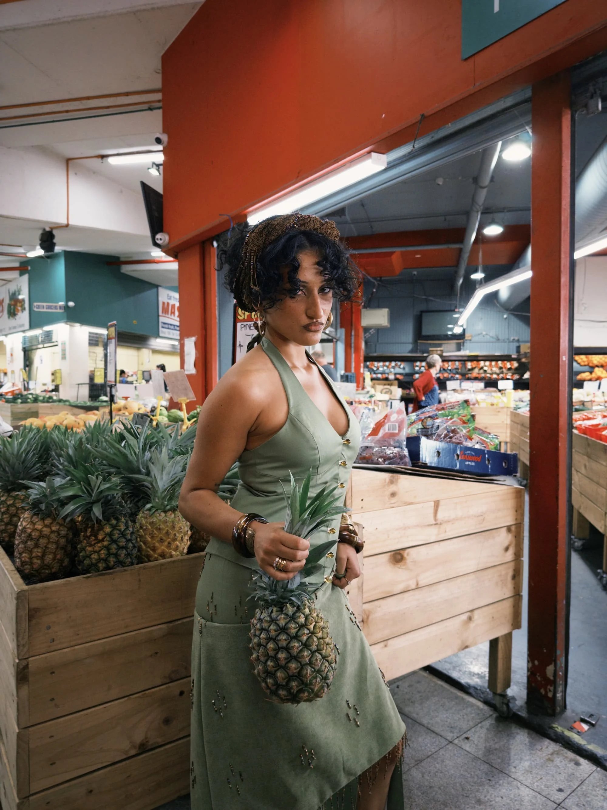 A person in the fruit and vegetable section of a market, holding a pineapple.