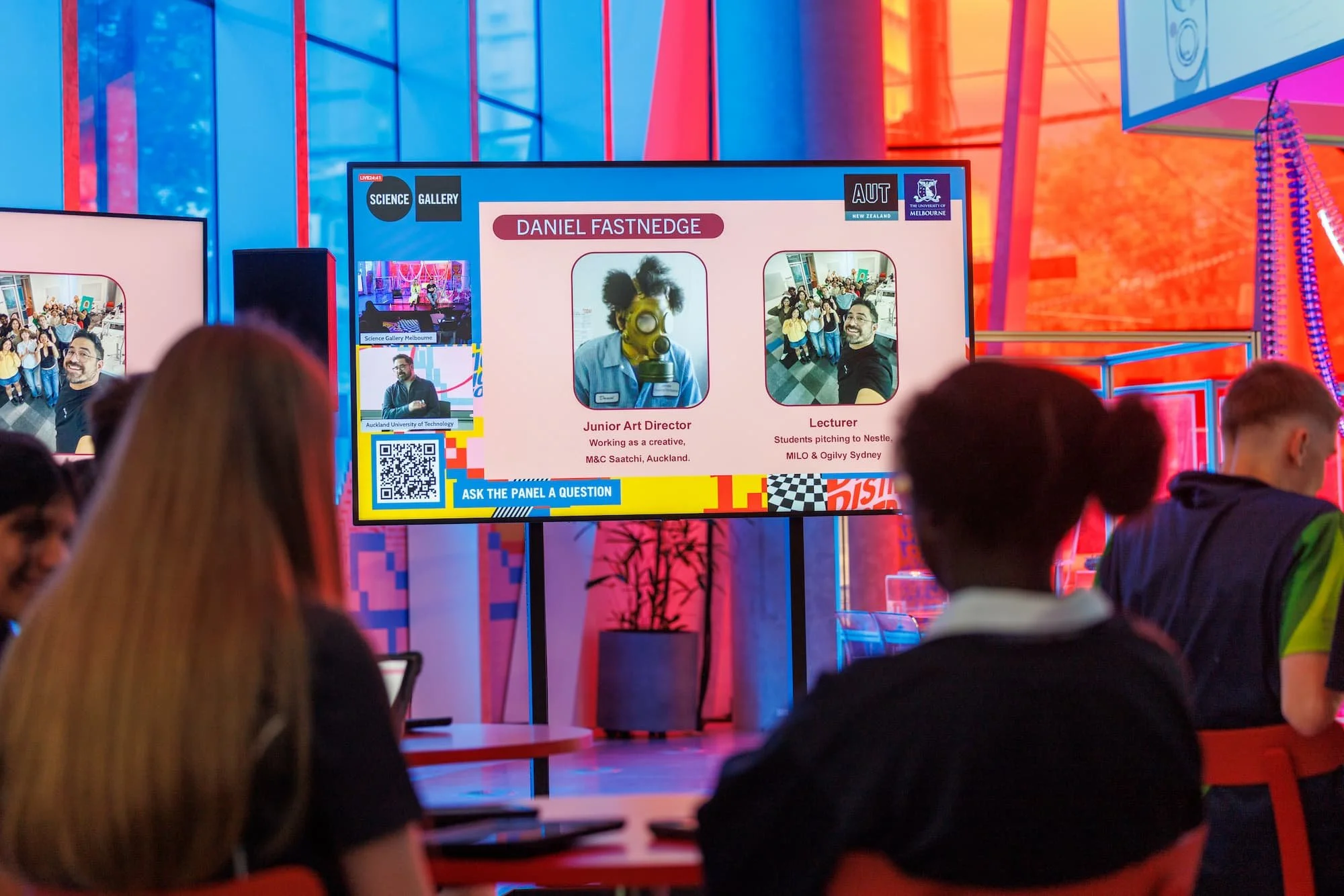 Students watching live stream video on a large tv in a colourful gallery space