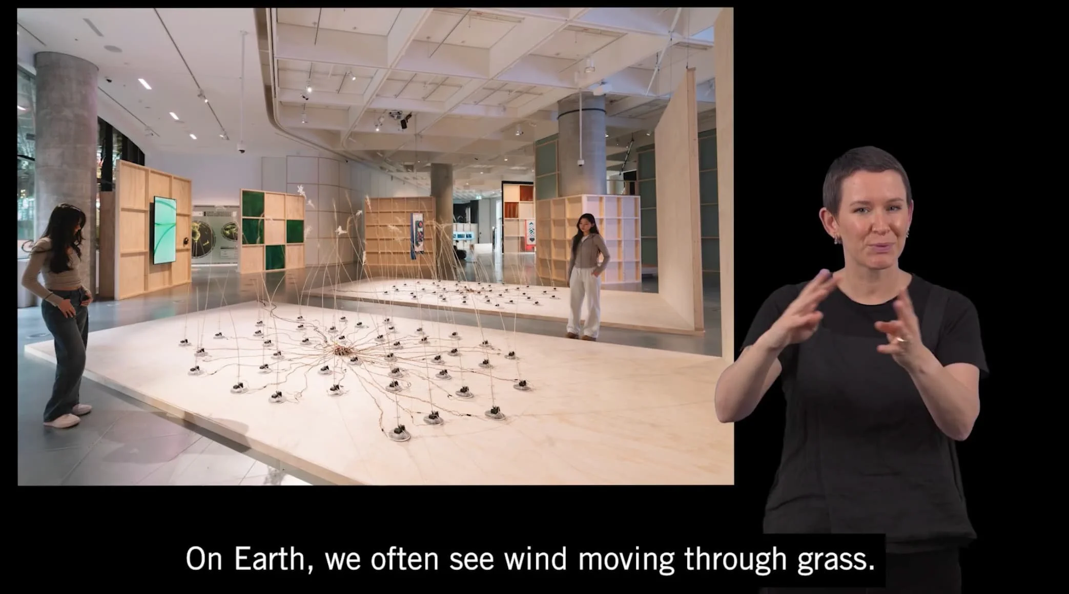 A person in a black t-shirt signs On earth, we often see wind moving with an image of two people looking at a sculpture in a gallery