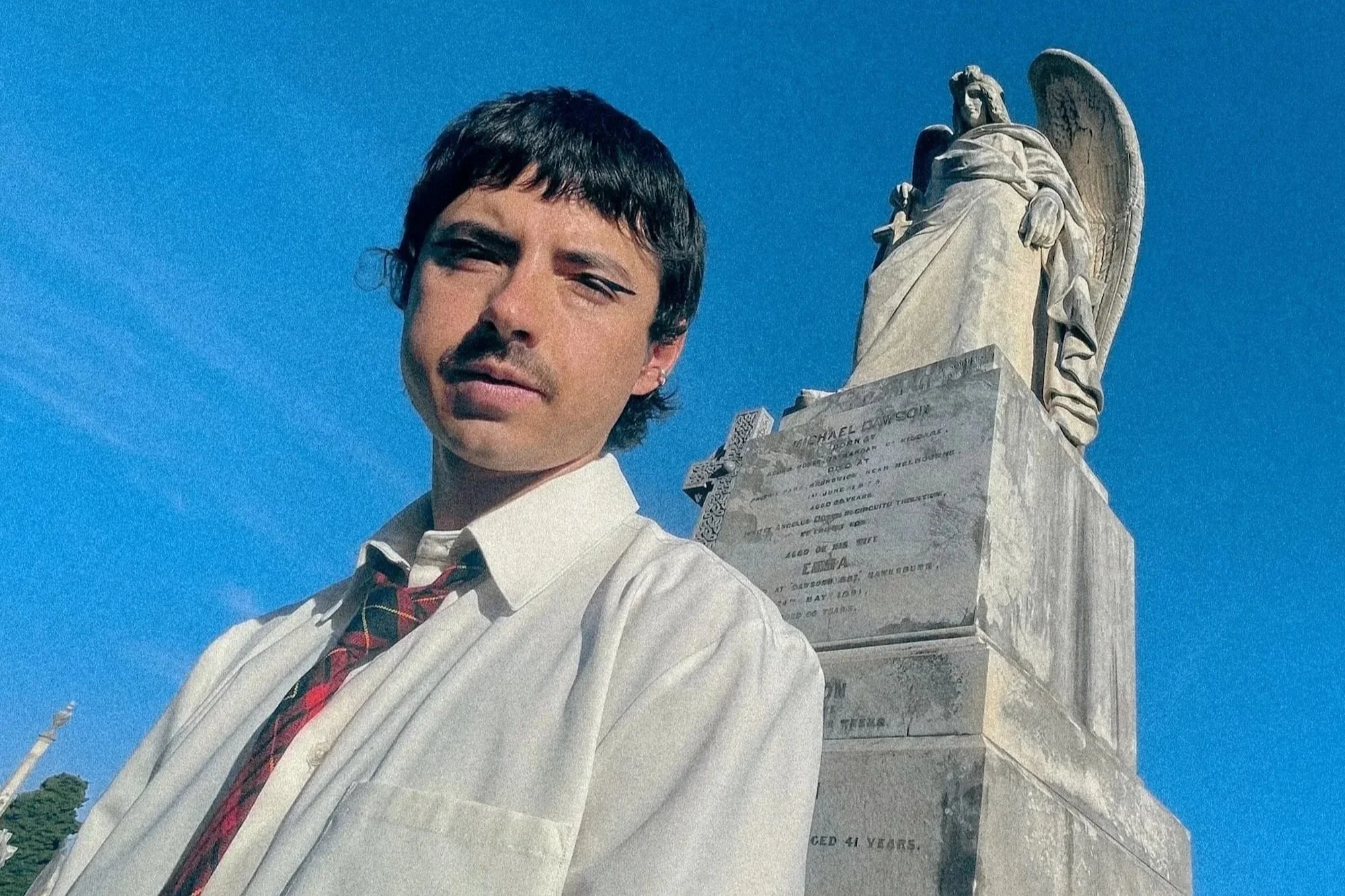 Photo taken from low perspective of artist standing in front of a memorial with an angel atop.