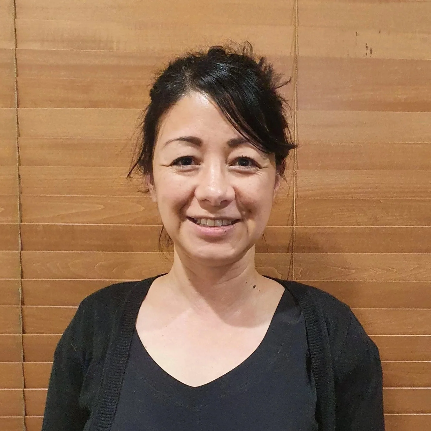 A woman with dark hair tied up, wearing a black top and black cardigan.