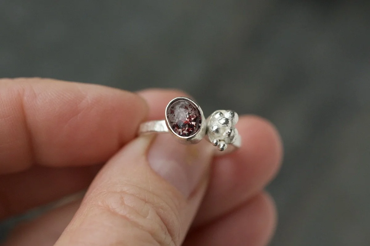 Fire quartz cabochon lichen cluster ring in a hand.jpeg