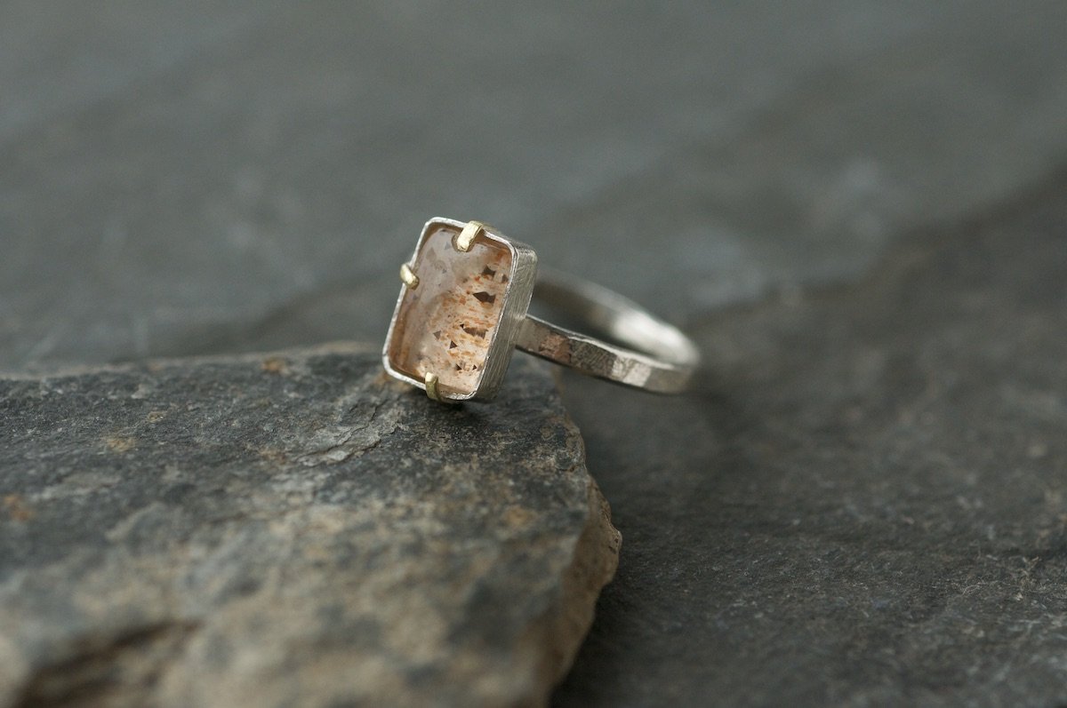Rainbow lattice sunstone rectangle ring with gold claw setting on slate.jpeg