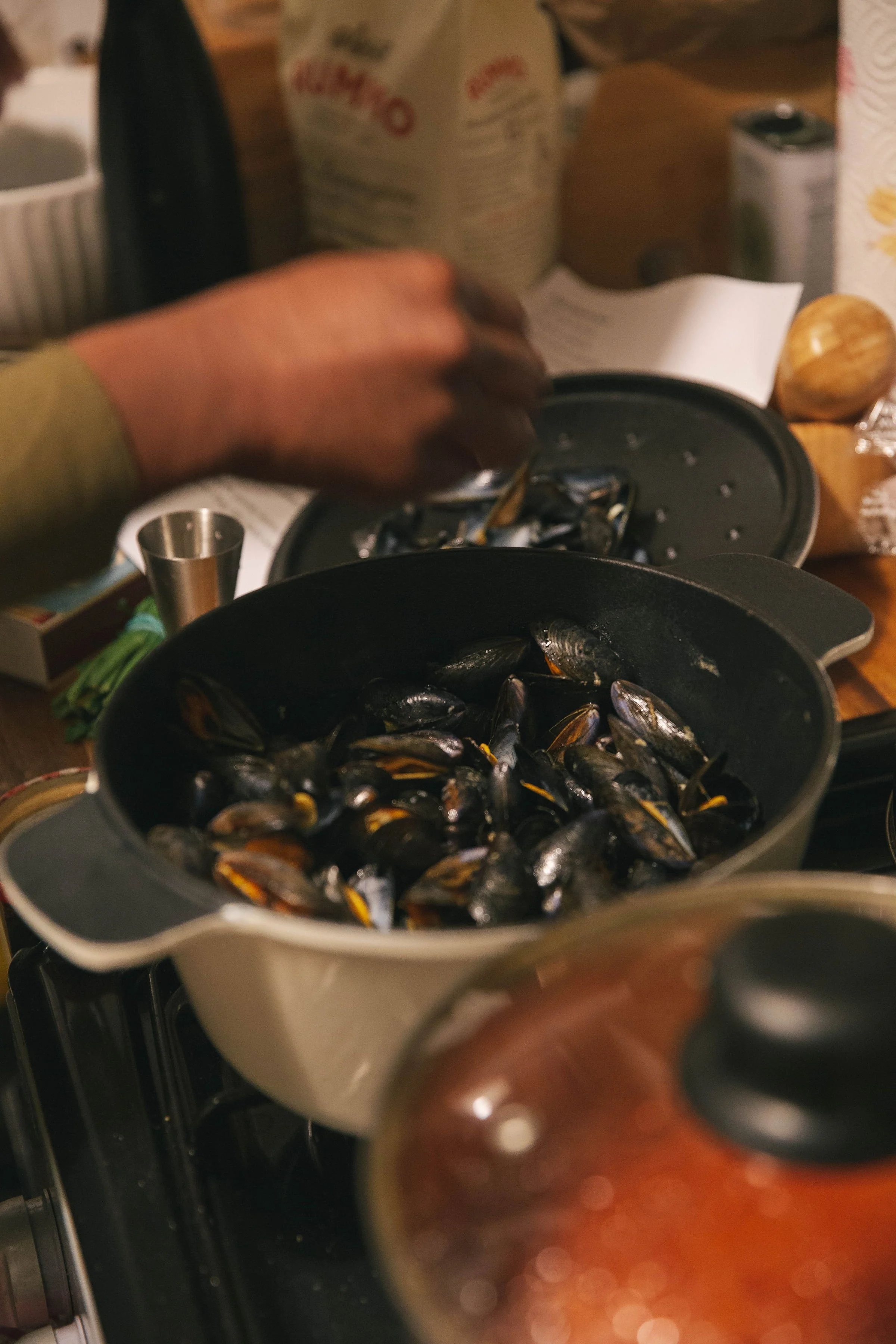 A person preparing mussels in a pot on a stove with various kitchen items in the background.